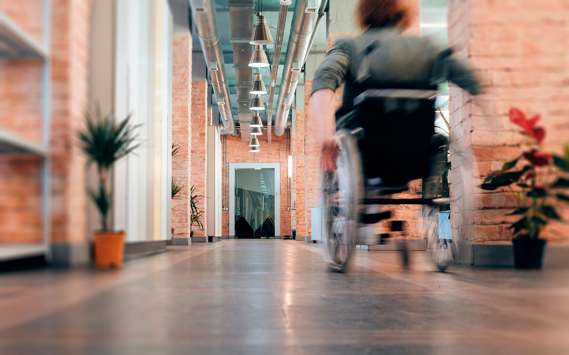Imagem desfocada (efeito de movimento) de uma pessoa de cadeira de rodas a percorrer um corredor.