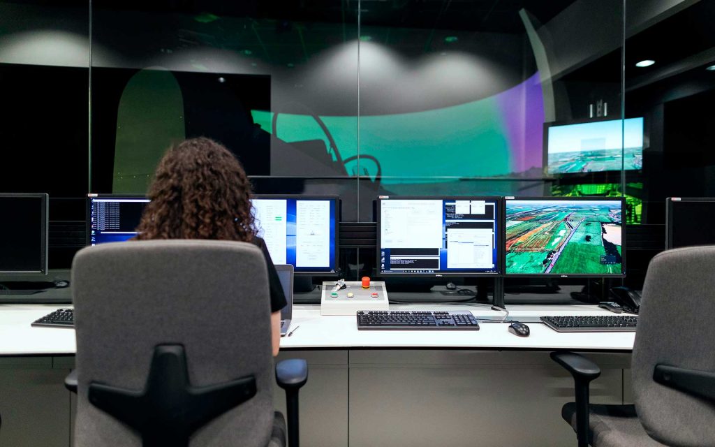 Mulher sentada numa secretária com vários computadores.